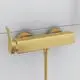 Brausearmatur in Brushed Gold-Finish von Ideal Standard, wandmontiert mit zwei Bedienelementen für Temperatur- und Wassermengenregulierung, an heller Wand installiert.
